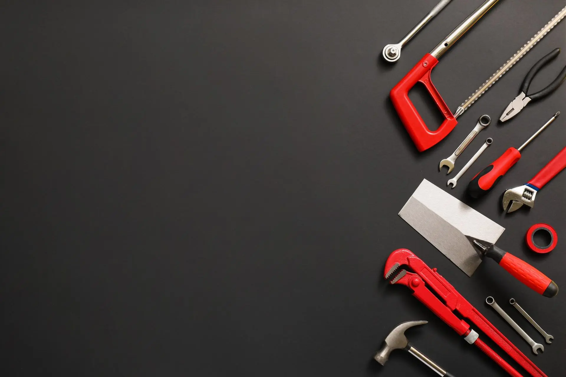 Hacksaw, wrenches, pliers, trowel, and hammer on a black surface
